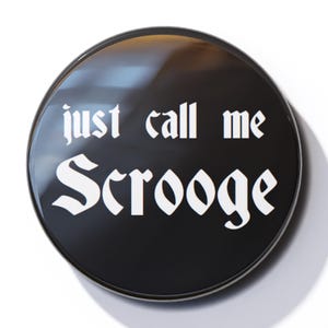 May include: A black button with a white inscription that reads "just call me Scrooge".