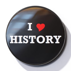 Puede incluir: Un botón negro con un borde blanco y el texto "I ♥ HISTORY" en letras blancas. El corazón es rojo.