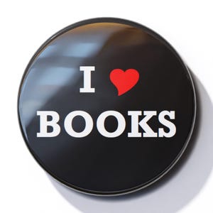 Könnte beinhalten: Ein schwarzer Knopf mit einer weißen Aufschrift, die "Ich liebe Bücher" lautet, und einem roten Herzen.
