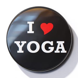 Könnte beinhalten: Ein schwarzer Knopf mit weißem Rand und dem Text "I ♥ YOGA" in weißen Buchstaben. Das Herz ist rot.