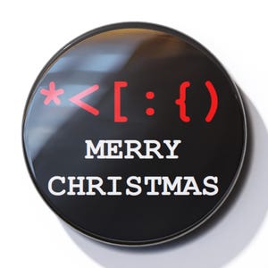 May include: A black round button with the text "* < [ : { } ] Merry Christmas" in red and white.