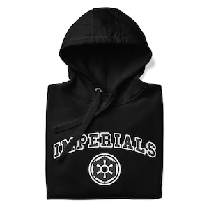 Puede incluir: Sudadera con capucha negra con la palabra "IMPERIALS" en letras blancas arqueadas. Debajo del texto hay un gráfico circular blanco. La sudadera tiene un cordón y una capucha.