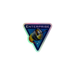 Pode incluir: Um adesivo triangular com borda hologr&aacute;fica, fundo azul escuro e a palavra ENTERPRISE em letras mai&uacute;sculas brancas. O design inclui uma antena parab&oacute;lica met&aacute;lica estilizada com um rastro de chama amarela e pequenas estrelas brancas.