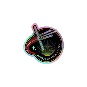 Könnte beinhalten: Ein kreisförmiger holografischer Aufkleber mit schwarzem Hintergrund und einer stilisierten Illustration eines Raumschiffs. Das Design enthält eine rote geschwungene Spur, einen kleinen vierzackigen Stern und den Text PROJECT HAIL MARY in weißen Großbuchstaben.