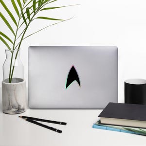 May include: A silver laptop computer with a black Star Trek insignia sticker on the lid. The sticker has a rainbow iridescent effect.