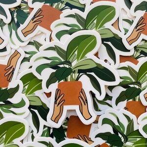 May include: A set of stickers featuring a hand holding a potted plant with green leaves. The stickers are printed on white paper and have a glossy finish.