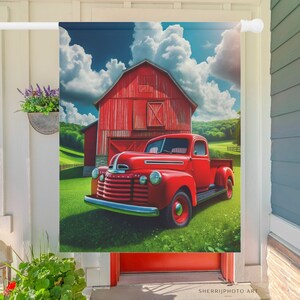 May include: A red vintage pickup truck parked in front of a red barn with a blue sky and white clouds in the background. The truck has a white cab and a white bed. The barn has a white door and a white window.