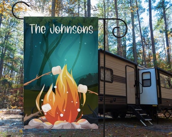May include: A personalized camping themed garden flag with the text "The Johnsons" and a cartoon illustration of a campfire with marshmallows roasting on sticks.