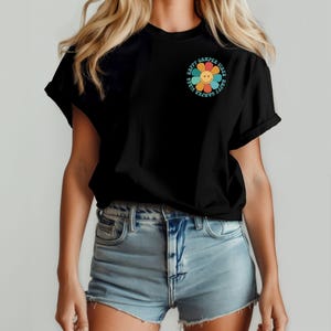 May include: Black t-shirt with a colorful flower graphic and the text "Happy Camper Vibes" around it.