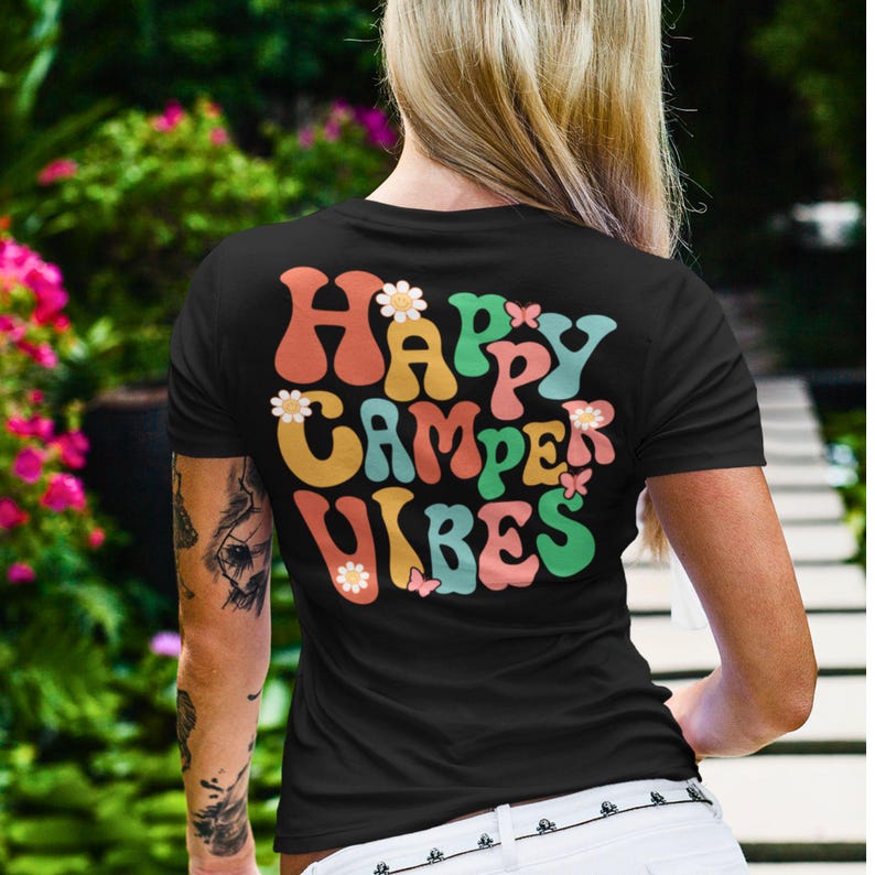 May include: Black t-shirt with a retro-style graphic that says "Happy Camper Vibes" in colorful letters with flowers and butterflies.