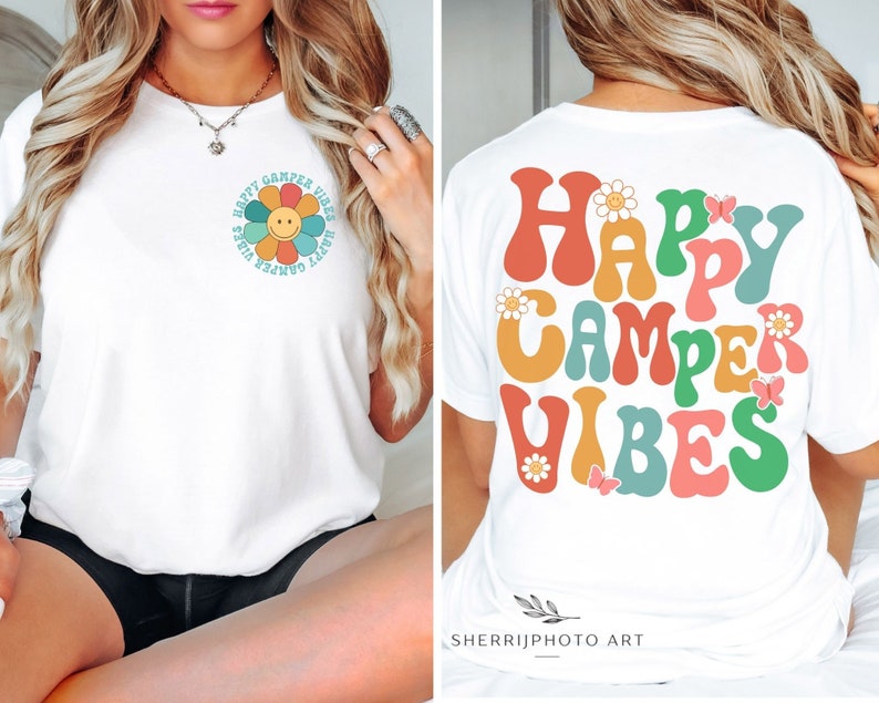 May include: White t-shirt with a colorful retro-style graphic that says "Happy Camper Vibes". The graphic features a daisy with a smiley face and butterflies.