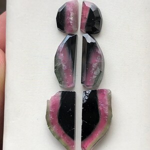 May include: Set of six gemstone cabochons, featuring a mix of black, pink, and green colors. The cabochons are cut in a variety of shapes, including ovals and half-ovals.