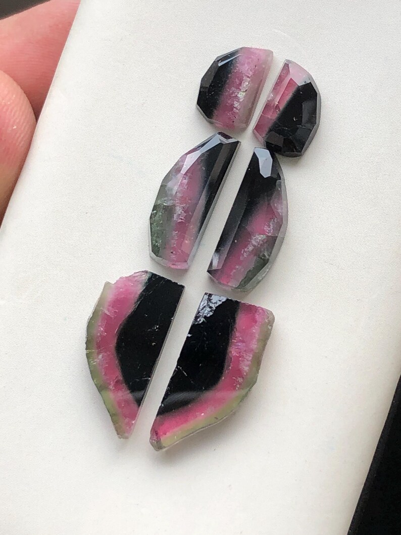 May include: Five gemstone cabochons in various shapes and sizes. The stones are a mix of black, pink, and green.