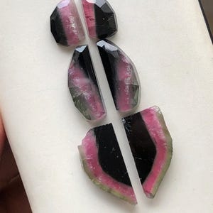 May include: Six pieces of pink, green, and black tourmaline gemstones. The gemstones are cut into irregular shapes and have a polished finish.