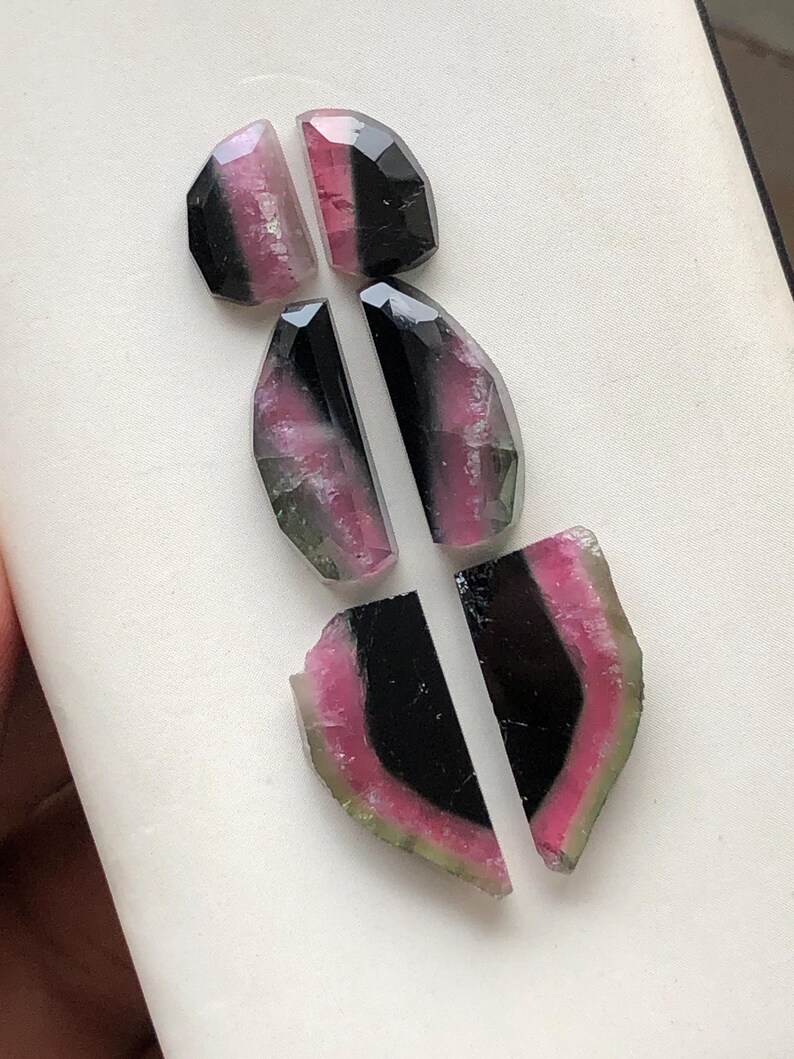 May include: Six pieces of pink, green, and black tourmaline gemstones. The gemstones are cut into irregular shapes and have a polished finish.