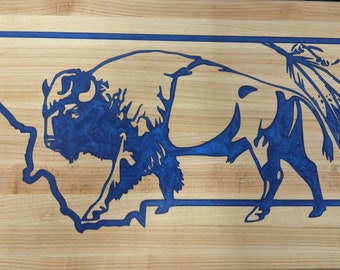 May include: A blue silhouette of a bison and a feather design inside the outline of the state of Montana on a wooden surface.
