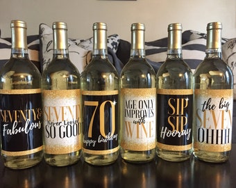 Peut inclure: Six bouteilles de vin avec des étiquettes noires et dorées. Les étiquettes ont des dictons différents liés à un 70e anniversaire. Les dictons incluent "Seventy & Fabulous", "Seventy Never Looked So Good", "70 Happy Birthday", "Age Only Improves with Wine", "Sip Sip Hooray", et "The Big Seven Ohhhh".