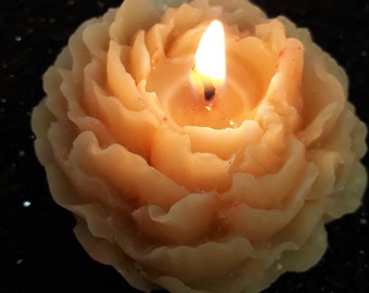 May include: A beige candle shaped like a rose with a single flame burning in the center.