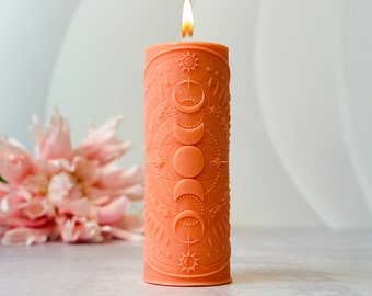 May include: A peach-colored candle with a detailed design of moons and stars. The candle is lit and the flame is visible.