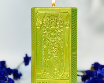 May include: Green candle with a gold metallic finish, featuring the High Priestess tarot card design. The candle is lit and has a flame on top.