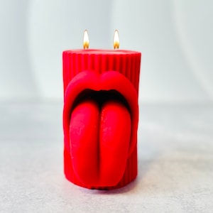May include: Red candle with a sculpted design of a mouth and tongue. The candle has two lit wicks.