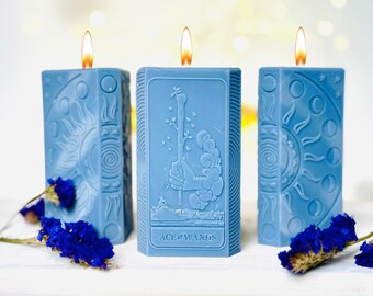 Puede incluir: Tres velas azules con diseños de cartas de tarot. La vela del medio tiene el texto "Ace of Wands" en la parte inferior.