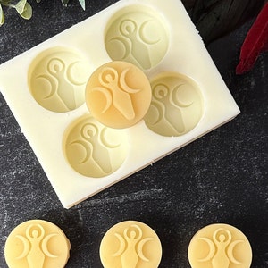 May include: A silicone mold with five circular impressions, each featuring a raised design of a woman standing with three crescent moons. There are four yellow wax melts with the same design, one of which is sitting on top of the mold.