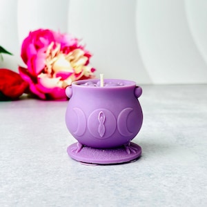 May include: Purple cauldron candle with a triple moon and goddess symbol. The candle is on a small purple base.