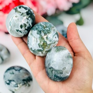 Puede incluir: Tres piedras de &aacute;gata verde y blanca pulidas en una mano. Las piedras son lisas y pulidas, con una variedad de patrones verdes y blancos.