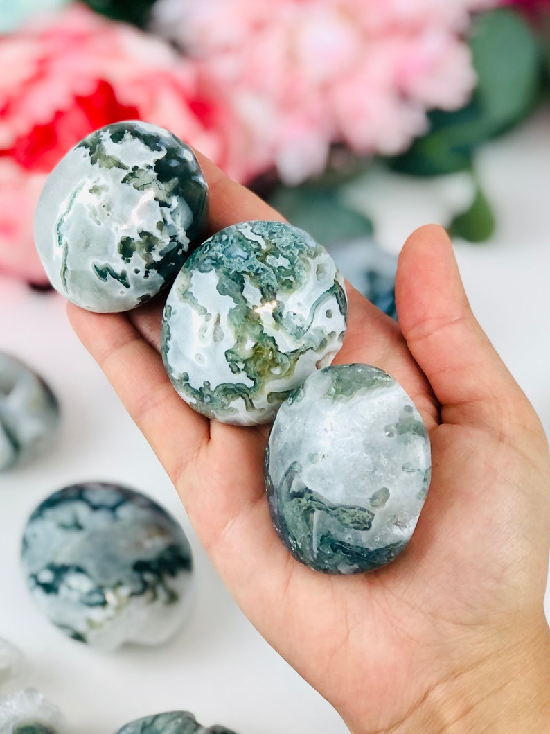 Puede incluir: Tres piedras de &aacute;gata verde y blanca pulidas en una mano. Las piedras son lisas y pulidas, con una variedad de patrones verdes y blancos.