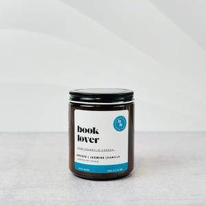 May include: A brown glass candle jar with a black lid. The label reads "book lover" and "orchid | jasmine | vanilla scented soy candle".