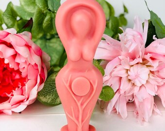 Puede incluir: Una vela rosa con forma de figura femenina con un diseño de árbol y un círculo en el centro. La vela está rodeada de flores rosas.