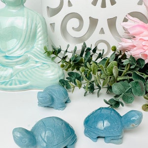 May include: Three blue-green stone turtle figurines on a white surface. The turtles are carved with detailed shells and faces.