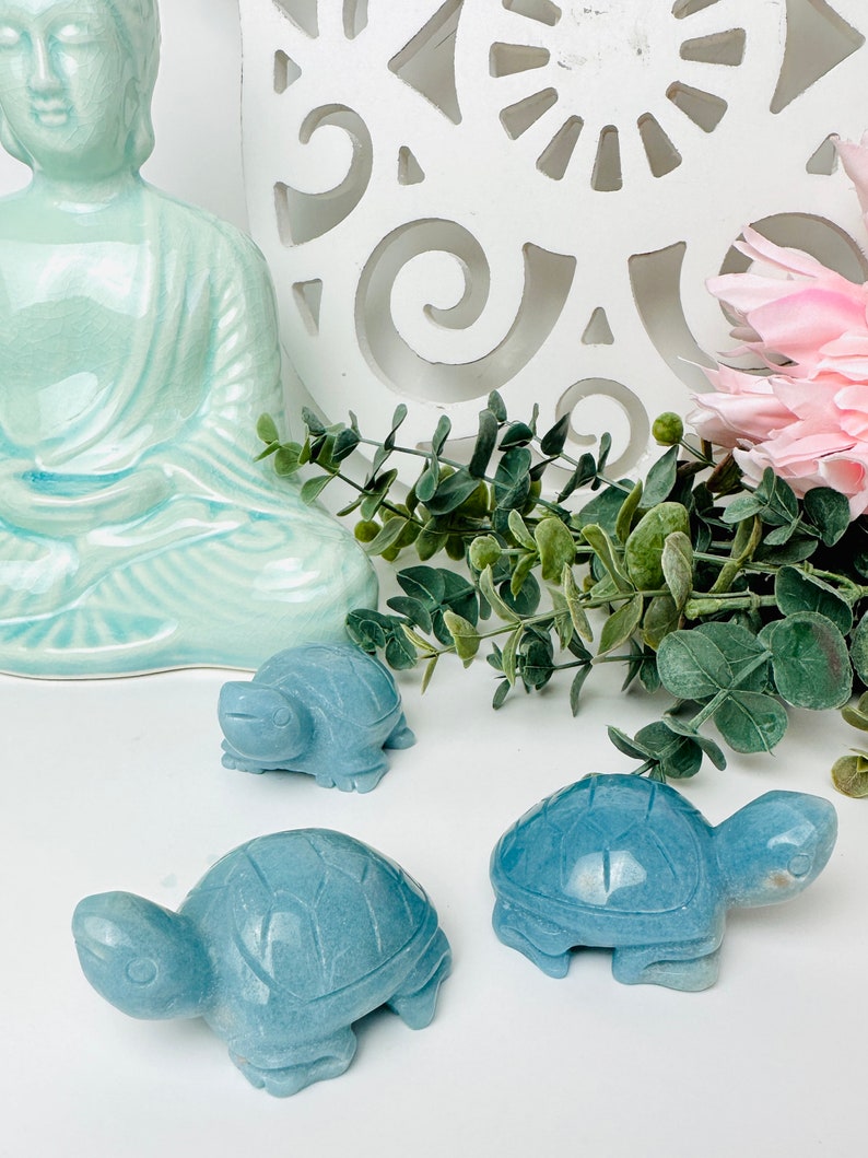 May include: Three blue-green stone turtle figurines on a white surface. The turtles are carved with detailed shells and faces.