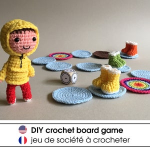 Op de afbeelding: Een gehaakt bordspel met een gele figuur met capuchon, kleurrijke gehaakte laarzen en een regenboogkleurige cirkel. Het spel heet "DIY crochet board game" in het Engels en "jeu de société à crocheter" in het Frans.