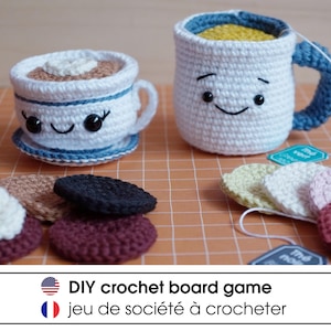 May include: A crochet set featuring a white teacup with a saucer, a white mug with a blue handle, and several small circular crochet pieces in various colors. The items have embroidered faces. Text at the bottom reads DIY crochet board game.