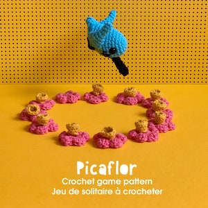 May include: A crochet game called "Picaflor" with a blue crocheted hummingbird and pink crocheted flowers. The game is a solitaire game.