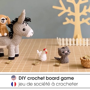 Puede incluir: Un juego de mesa de crochet DIY con un burro gris, un perro marrón, un gato gris, una gallina blanca y una cesta marrón con monedas de oro. El juego se titula "DIY crochet board game" en inglés y "jeu de société à crocheter" en francés.