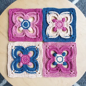 May include: Four crocheted squares in pink, blue, and cream colors. Each square features a floral design with a central circle.