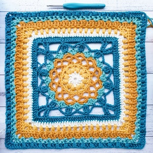 May include: A crocheted square featuring a geometric design in shades of blue, yellow and white. The square is worked using a variety of stitches, including single crochet, double crochet and treble crochet.