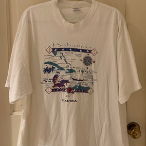 Puede incluir: Camiseta blanca con un estampado gráfico de un mapa de las Bahamas. El mapa incluye las islas de Abaco, Andros, Eleuthera, Exuma y Long Island. El texto "Bahamas" está impreso en azul sobre el mapa.