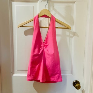 May include: A bright pink halter top with a deep V-neckline and a gathered detail at the bust.