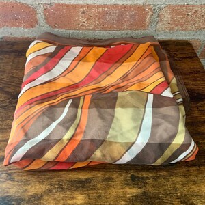 May include: A folded brown, orange, and white striped scarf with a geometric pattern.