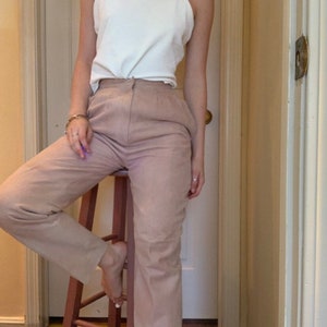 May include: A person wearing a white tank top and light pink pants. The pants have a high waist and a straight leg.