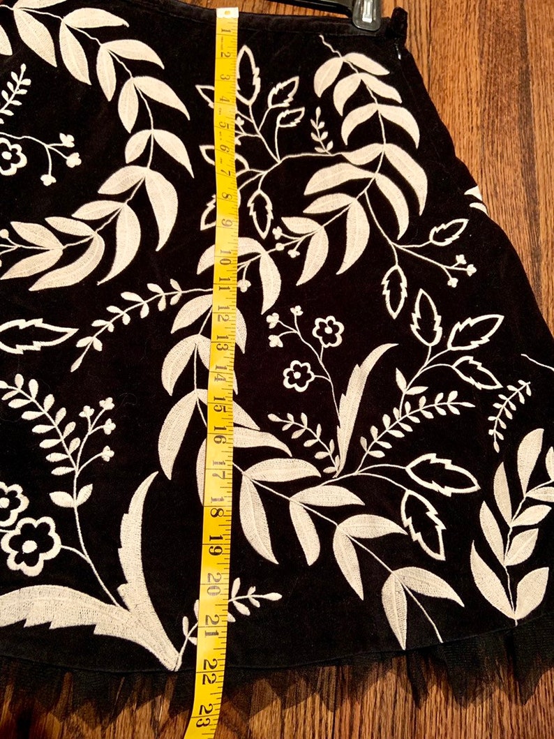 May include: Black skirt with a white floral embroidery design. The skirt has a tulle ruffle at the hem and measures approximately 23 inches in length.