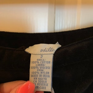 May include: A white tag with black text attached to a black garment. The tag reads "odille 2 SHELL: 100% COTTON LINING: 100% VISCOSE TRIM: 100% NYLON MADE IN INDIA RN 66170 CA 32054 TE REVERSE OR CARE"
