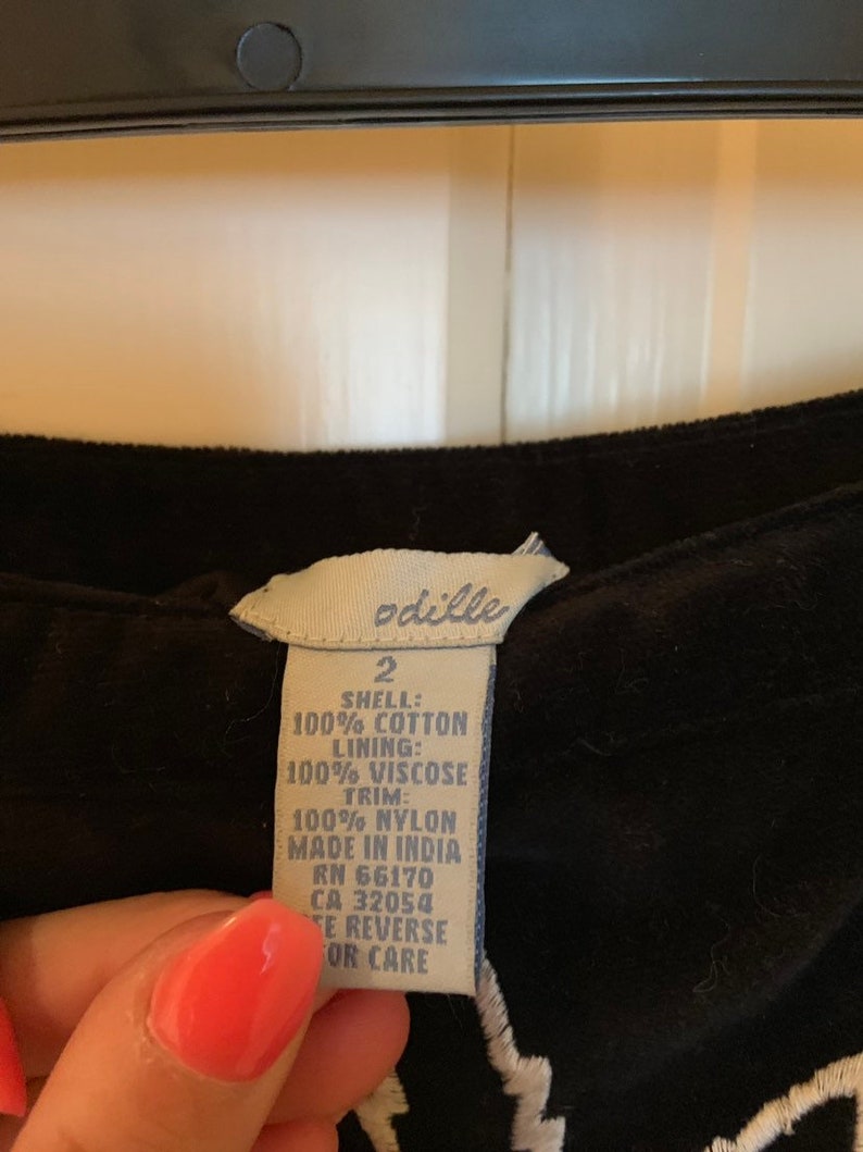 May include: A white tag with black text attached to a black garment. The tag reads "odille 2 SHELL: 100% COTTON LINING: 100% VISCOSE TRIM: 100% NYLON MADE IN INDIA RN 66170 CA 32054 TE REVERSE OR CARE"