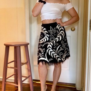May include: A black and white floral skirt with a white lace trim. The skirt is knee-length and has a fitted waist.