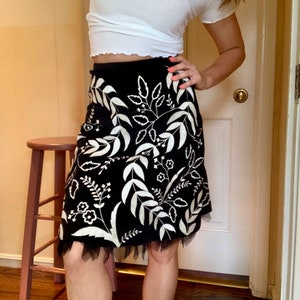 May include: A black skirt with a white floral pattern and a tulle trim. The skirt is knee-length and has a fitted waist.