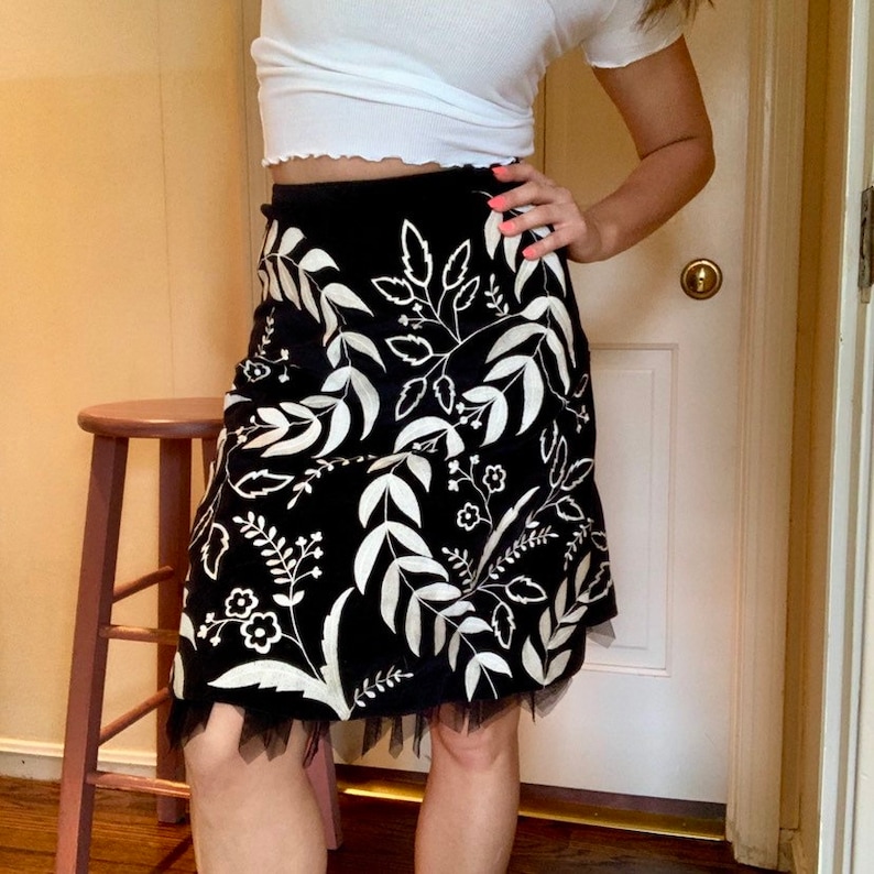 May include: A black skirt with a white floral pattern and a tulle trim. The skirt is knee-length and has a fitted waist.